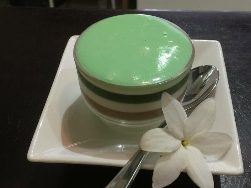 A layered green dessert in a glass with a frangipani