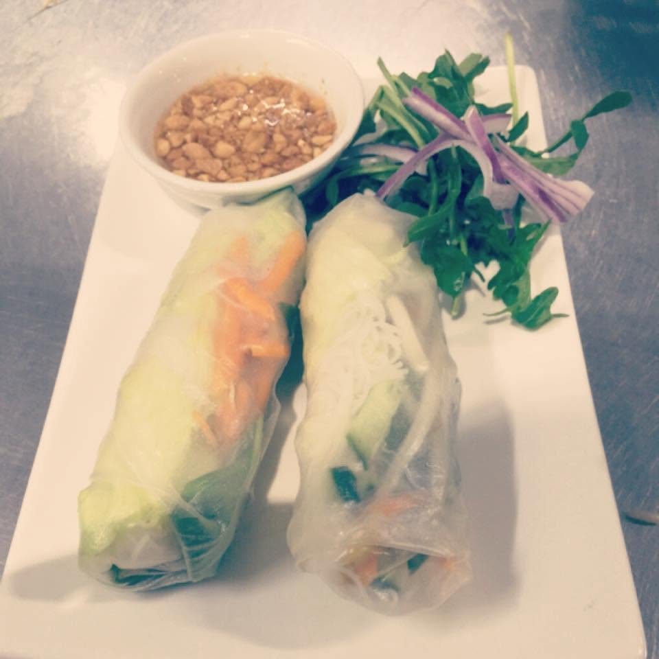 Two fresh rice paper rolls with herbs and a dish of peanuts