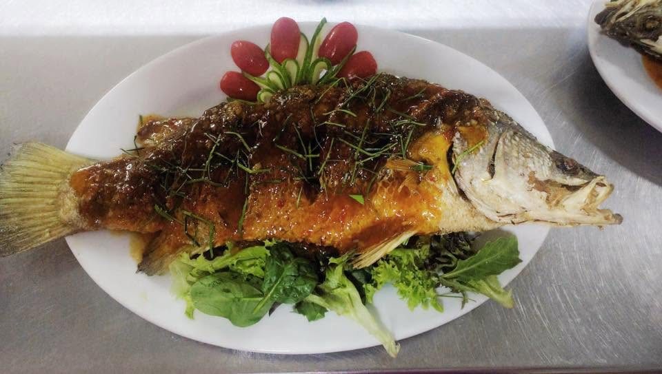 A whole fried fish topped with sauce and herbs on lettuce